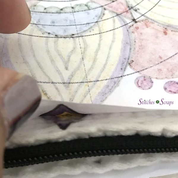 A finger lifts a corner of paper to reveal image transferred onto white pencil case. Personalized pencil case on Stitches n Scraps