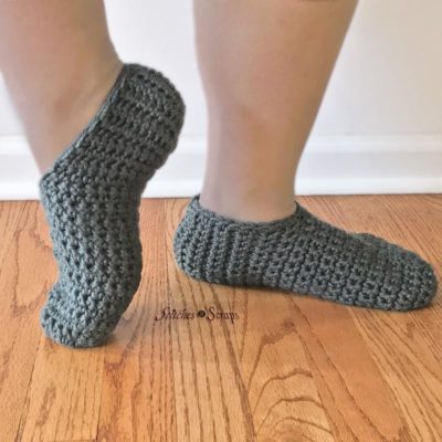 Woman's ankles and feet, wearing Simply Slippers. One foot is flat on the wood floor, the other is up on the toe and turned sideways. Simply Slippers - free crochet pattern on Stitches n Scraps