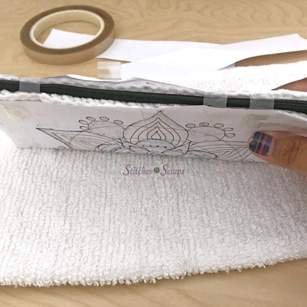 A piece of paper with a drawing on it is taped around a pencil case, resting on a white towel on top of a wood table. In the background are some paper scraps and some heat resistant tape. Personalized Pencil Case on Stitches n Scraps