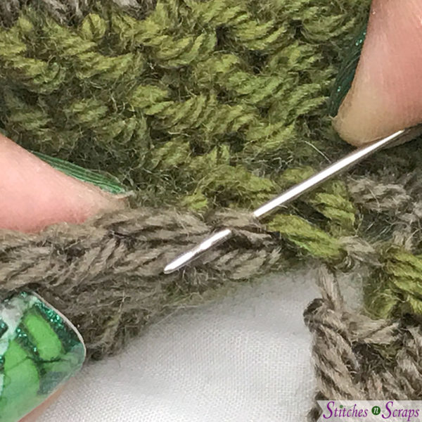 Taupe and green striped fabric. Hands inserting a yarn needle through a loop a the edge of one piece.