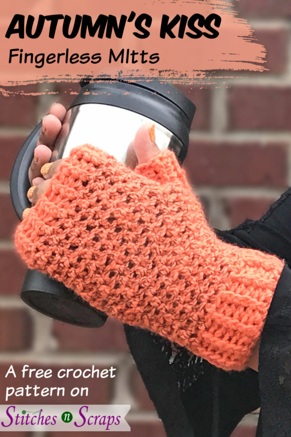 hands wearing orange and black, crocheted fingerless mitts, and holding a travel coffee mug. A red brick wall in the background. Autumn's Kiss easy crochet fingerless mitts. Free pattern on Stitches n Scraps