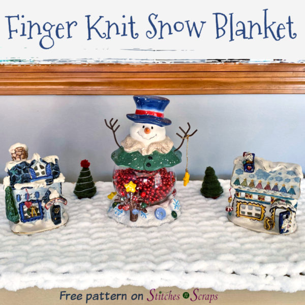 A finger knit snow blanket, with some holiday decorations on top of it. Text - Finger Knit Snow Blanket - Free Pattern on Stitches n Scraps