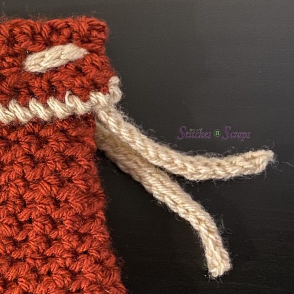 A crochet swatch with a folded top layer. A drawstring is woven in such that it sticks out between the layers