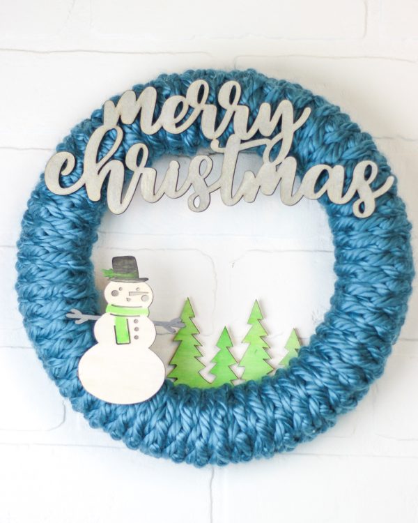 A simple crocheted wreath with a snowman and trees on it. Crochet Wreath for Beginners from Winding Road Crochet