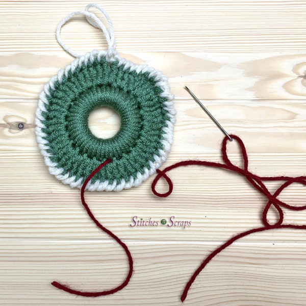A crocheted Christmas wreath with a piece of red yarn attached