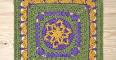 Crocheted Supernova afghan block on a wood table. Wording says Supernova Square a free crochet pattern on Stitches n Scraps