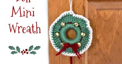 A mini crochet Christmas wreath hanging on a door. Text says Jingle Bell Mini Wreath - Free crochet pattern on Stitches n Scraps
