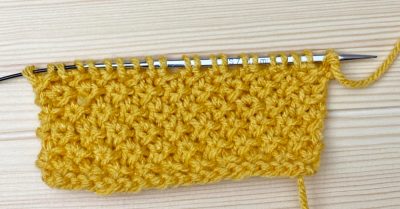 A knitted swatch on a wood table - Rosette Stitch - Knitting Tutorial on Stitches n Scraps