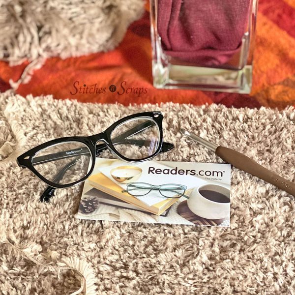 glasses on a background of fur yarn, with a crochet hook and Readers.com postcard